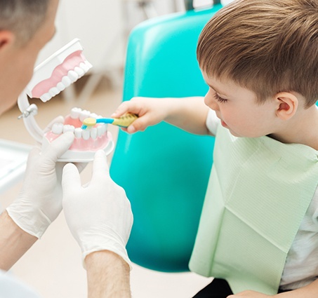 Dentist helping young boy practice toothbrushing at children's dentistry visit