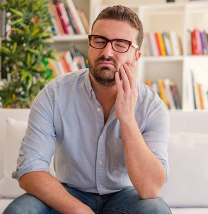 man sitting on a couch and holding the side of his face in pain 