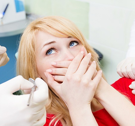 Woman in need of sedation dentistry covering her mouth in fear