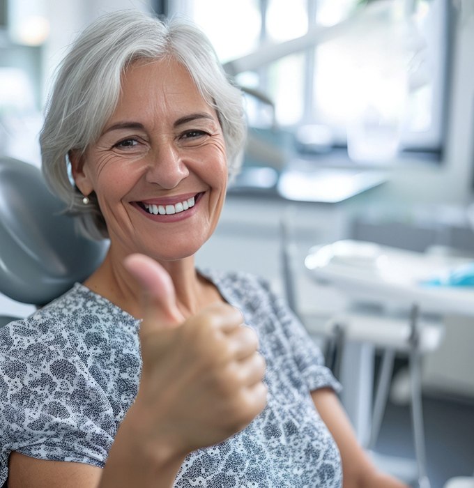 Older woman smiling and giving a thumbs up in the dentist’s chair