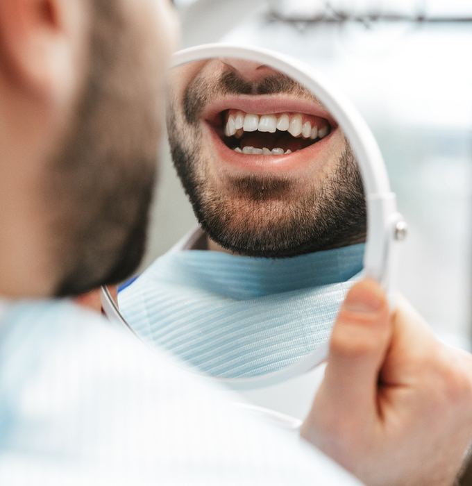 Man’s smile with chipped tooth reflected in mirror