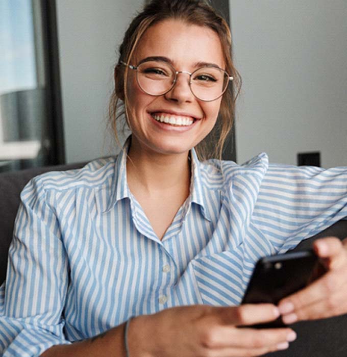 Woman with phone smiling with dental implants in Muskegon, MI